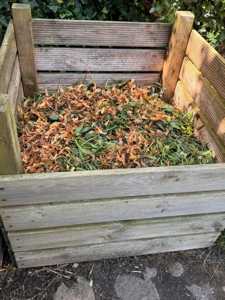 Ein selbstgebauter Kompostbehälter aus Holz ist mit einem Mix aus grünen und braunen organischen Küchen- und Gartenabfällen gefüllt.